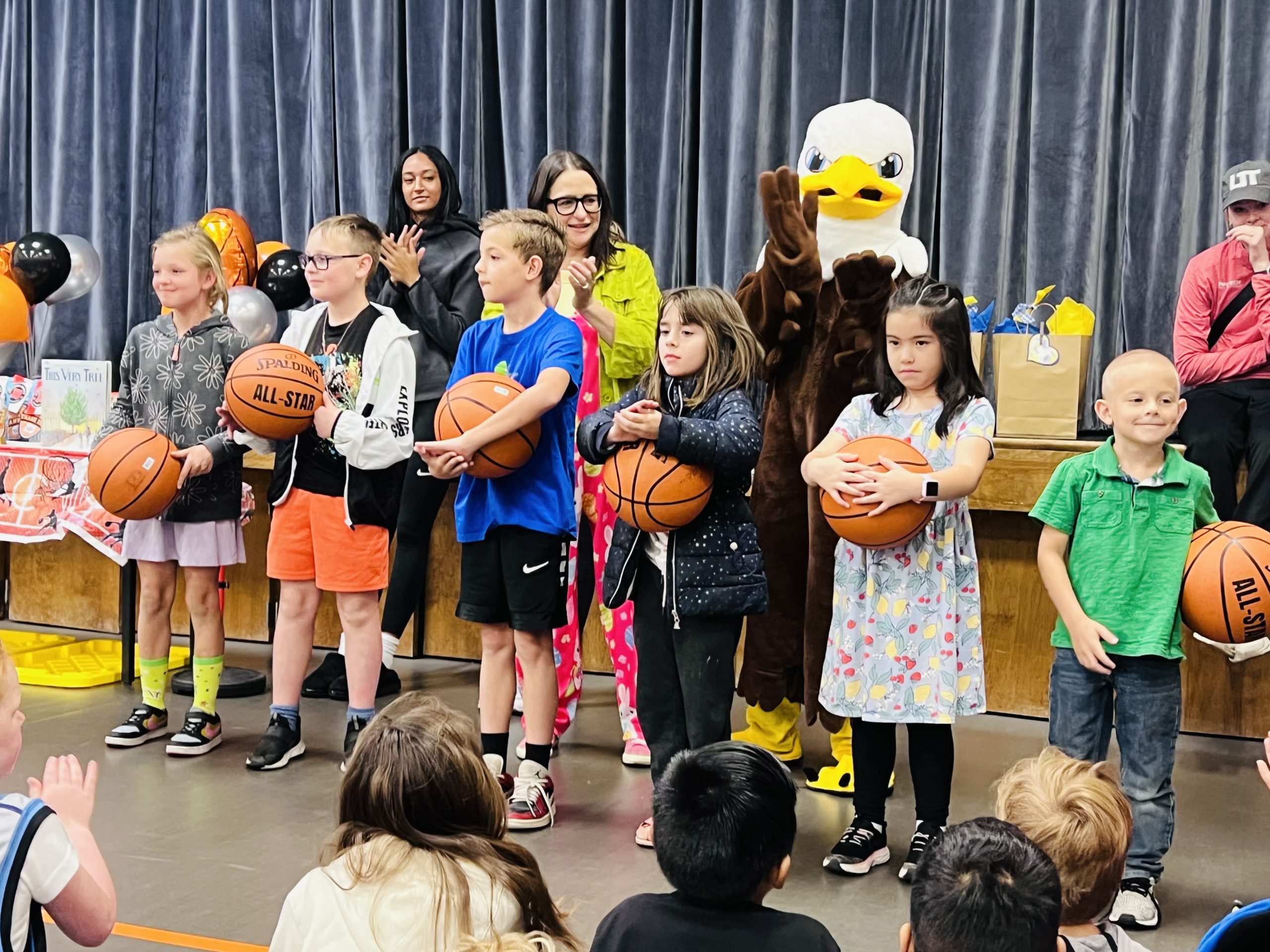 Students standing in the front of the gym with a signed basketball from Utah Tech for being awesome readers